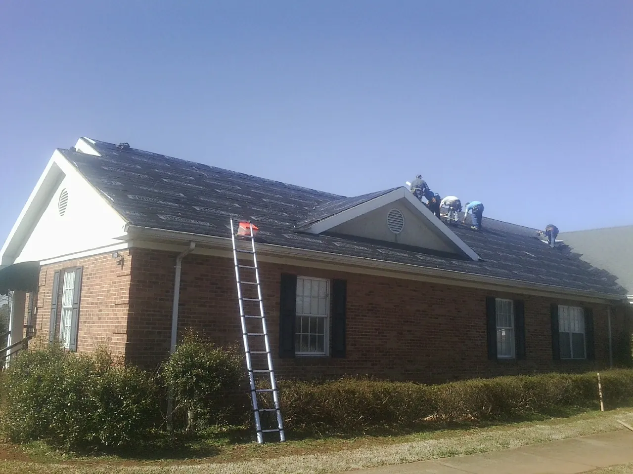 Crew tearing shingles off a brick ranch roof with a ladder set — Metal Roof Repair work by our crew in Clear Spring