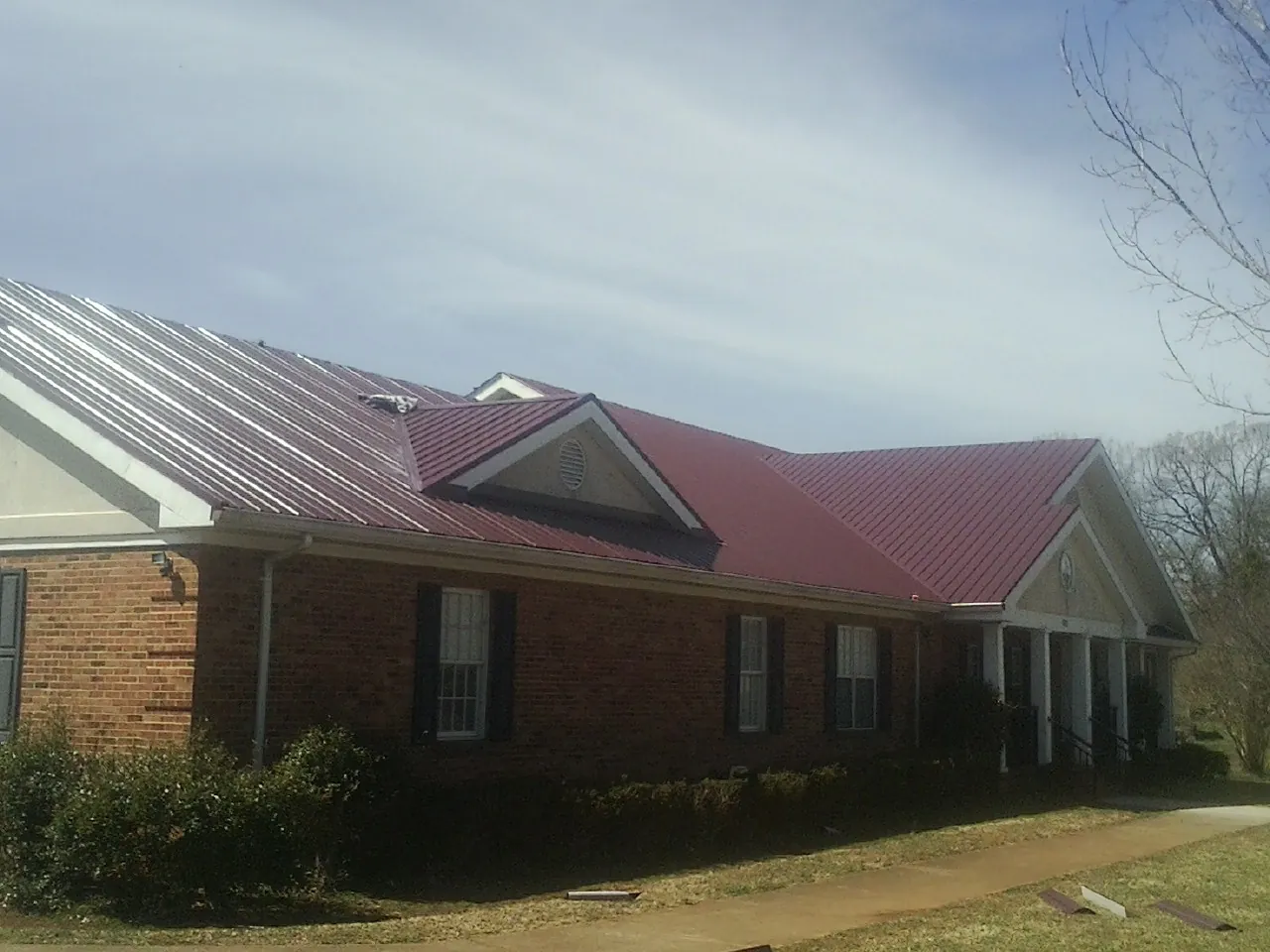 Red metal roof with gabled entries on a long brick building, from a Hail Damage Roof Repair job in Clear Spring