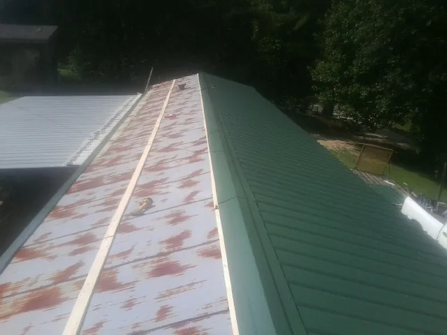 Old rusted panels beside newly installed green metal roofing — Wind Damage Roof Repair by Roofing Brothers in Clear Spring