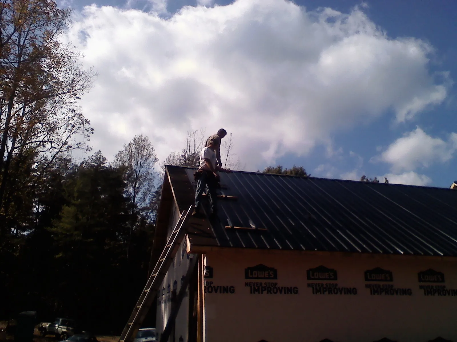 Roofer fastening dark metal panels high against a cloudy sky, from a Roof Inspection job in Clear Spring